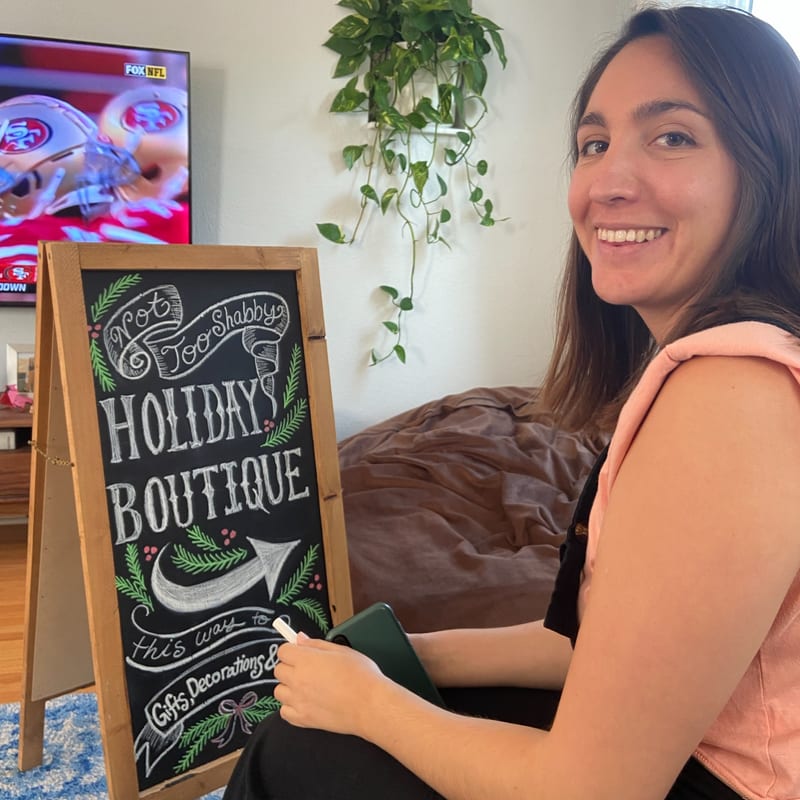 Nicole smiling beside a hand-lettered holiday boutique chalkboard sign