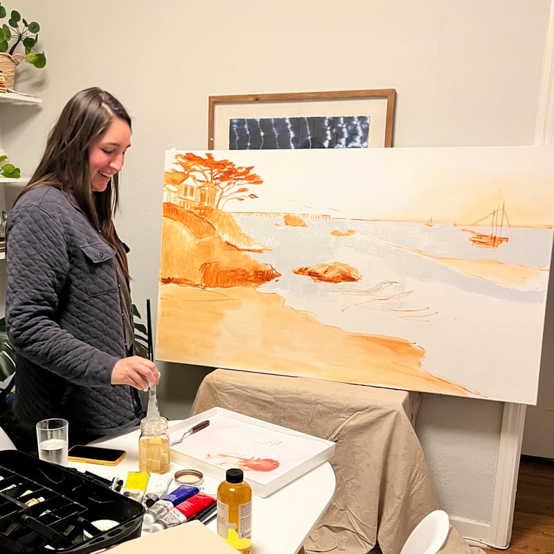 Nicole painting a coastal scene on an easel