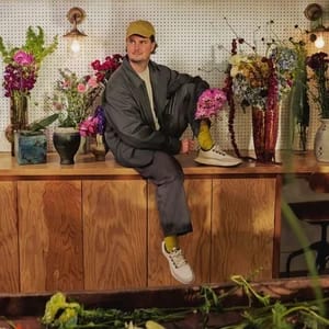 A man sitting on a counter surrounded by flowers wearing allbirds sneakers