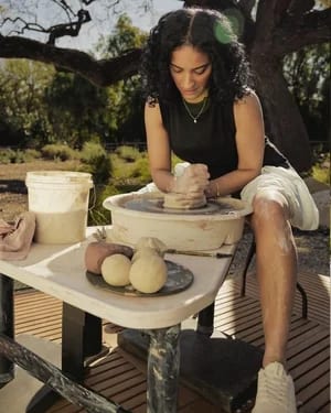 A woman working clay on a pottery wheel outdoors wearing allbirds sneakers