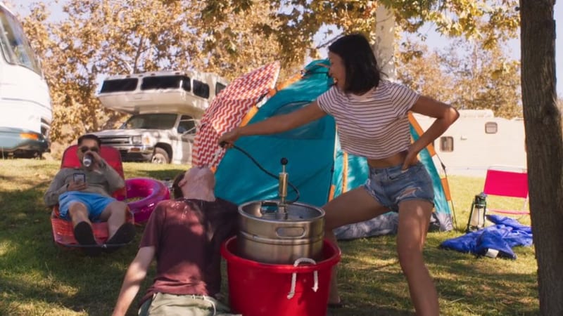 A girl pumping a beer keg at a campsite
