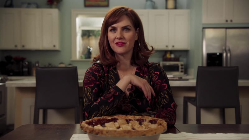 A woman sitting at a kitchen table with a freshly baked pie