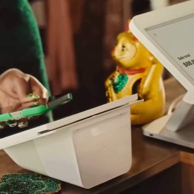 A hand tapping a phone against a Clover payment terminal at checkout