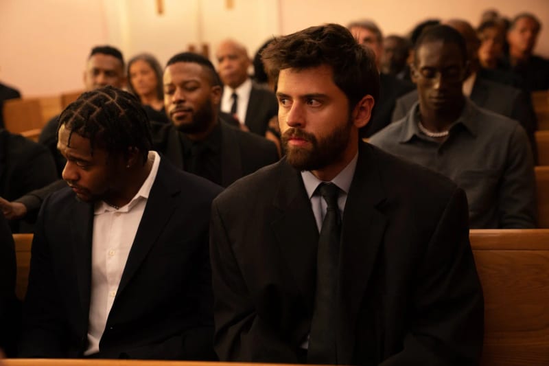 Hal seated in a church pew among mourners