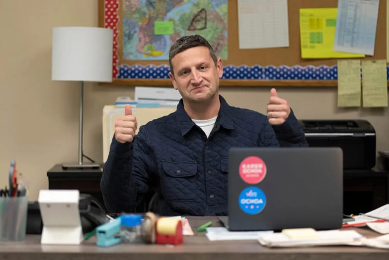 A man giving two thumbs up at a desk with campaign stickers on his laptop