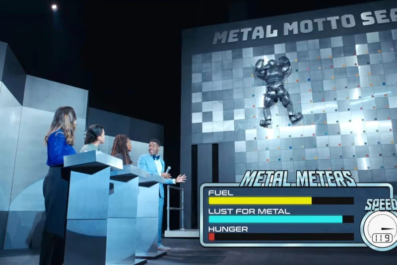 A game show set with contestants and a robot on a metal wall