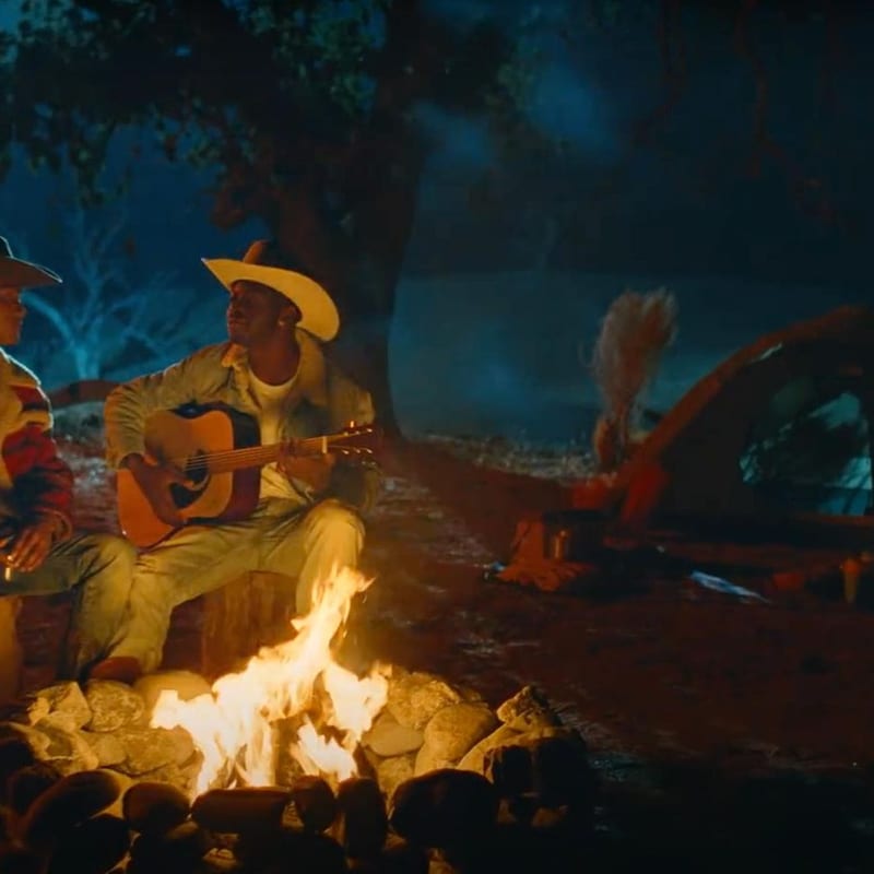 Two cowboys sitting by a campfire at night with a tent in the background