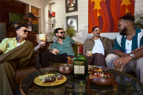 Four friends gathered around a table with Buchanan’s Deluxe and appetizers