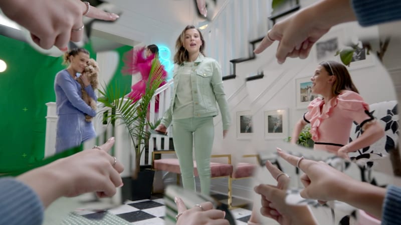 A woman surrounded by pointing hands in a colorful hallway set