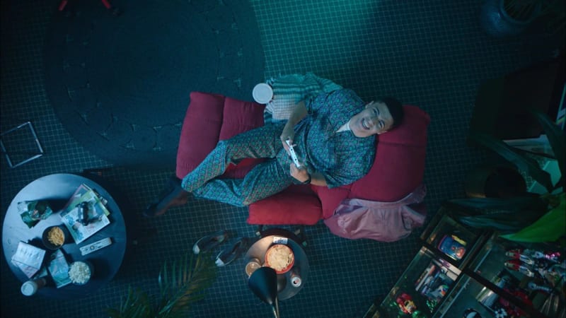 Overhead shot of a man laughing on a red couch surrounded by snacks