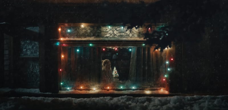 A woman seen through a snowy Christmas-light-framed window