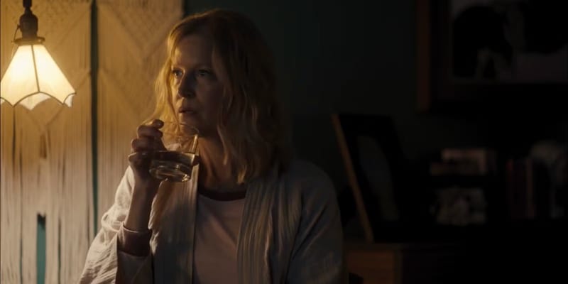 A woman drinking a glass of whiskey under a macrame lamp