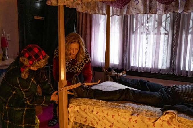 Two people standing over a body laid on a canopy bed